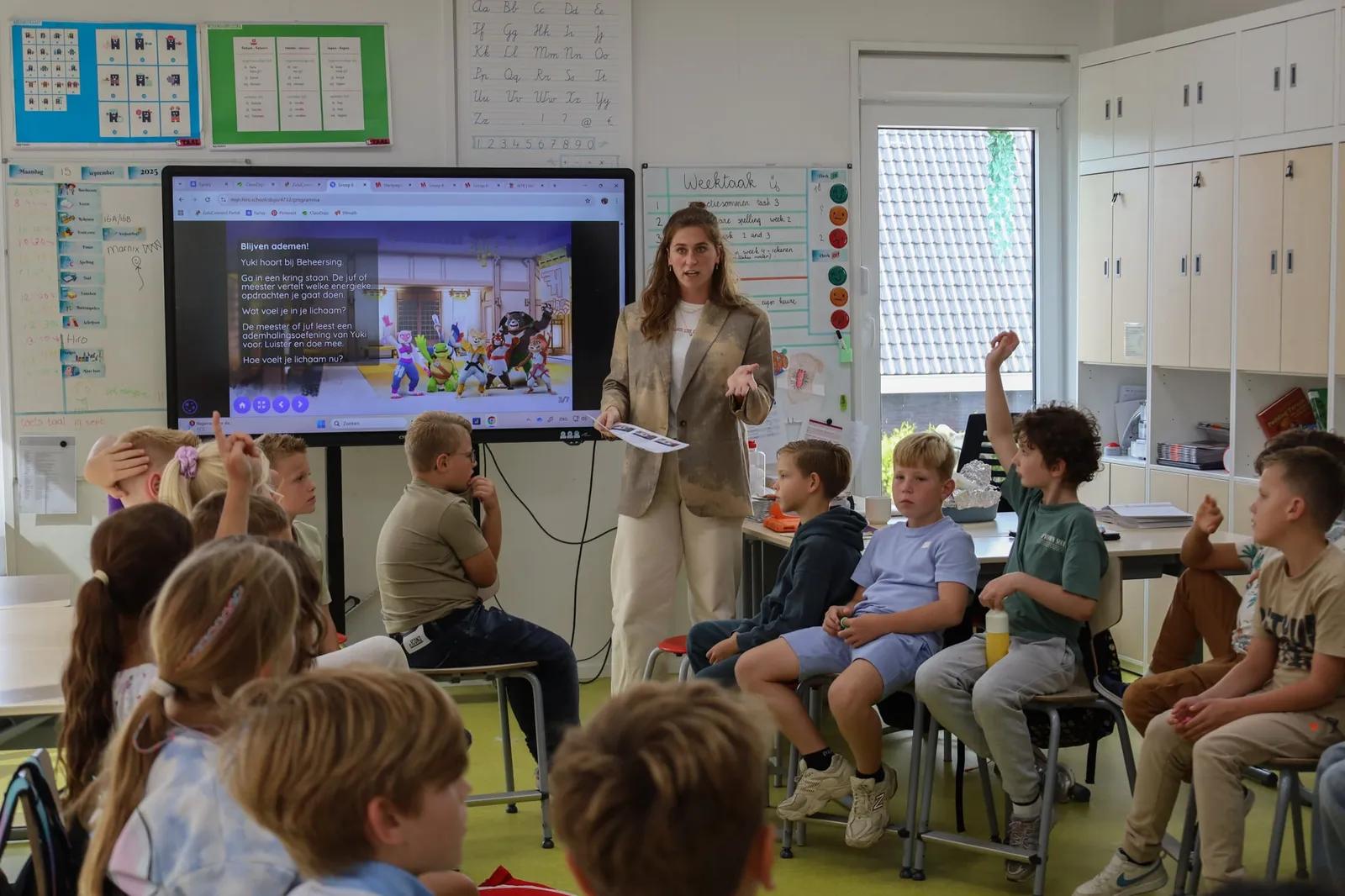 Leerkracht geeft een HiRO les terwijl kinderen enthousiast hun vinger opsteken